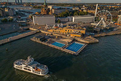 People swimming at Allas Sea Pool with ferries in background